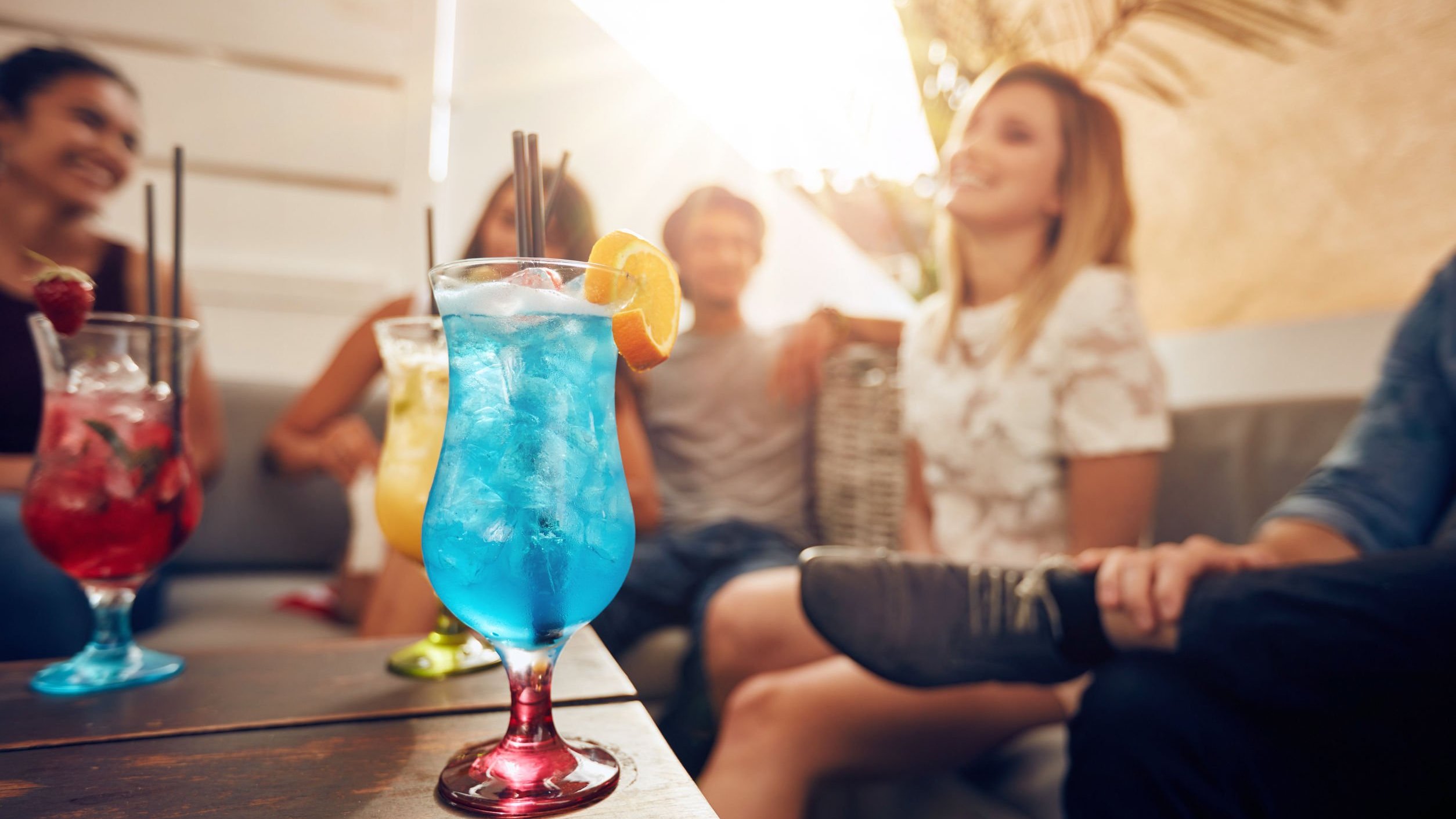 Grupo de pessoas sentadas num sofá, e mesa de centro com drinks coloridos.