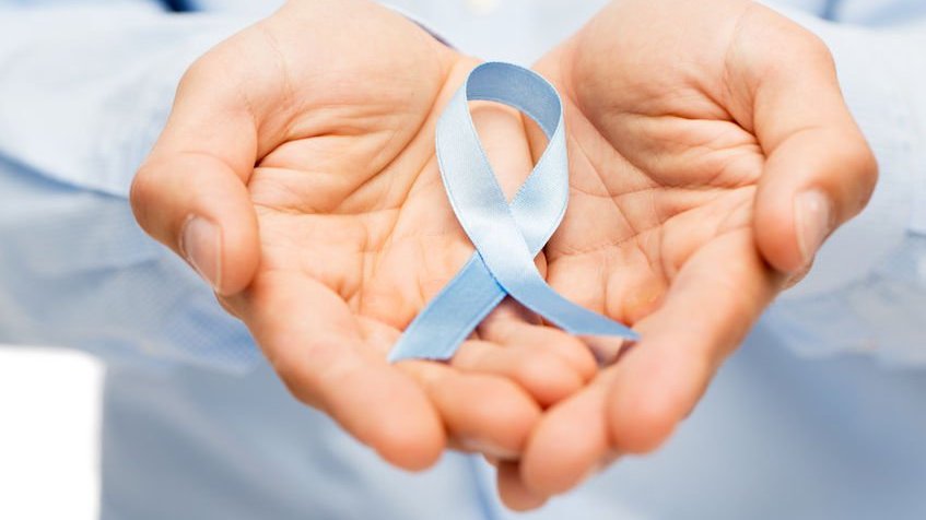 mãos masculinas segurando uma fita azul de conscientização do câncer de próstata