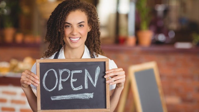 Mulher segurando um quadro escrito open (aberto, em inglês)