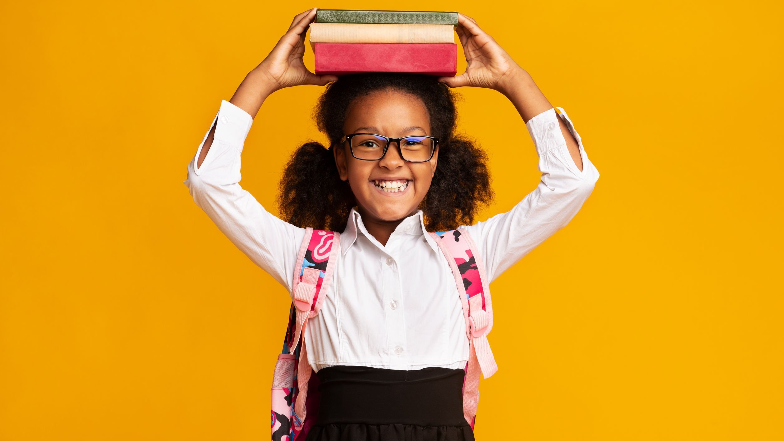 Garota sorridente segura livros sobre a própria cabeça