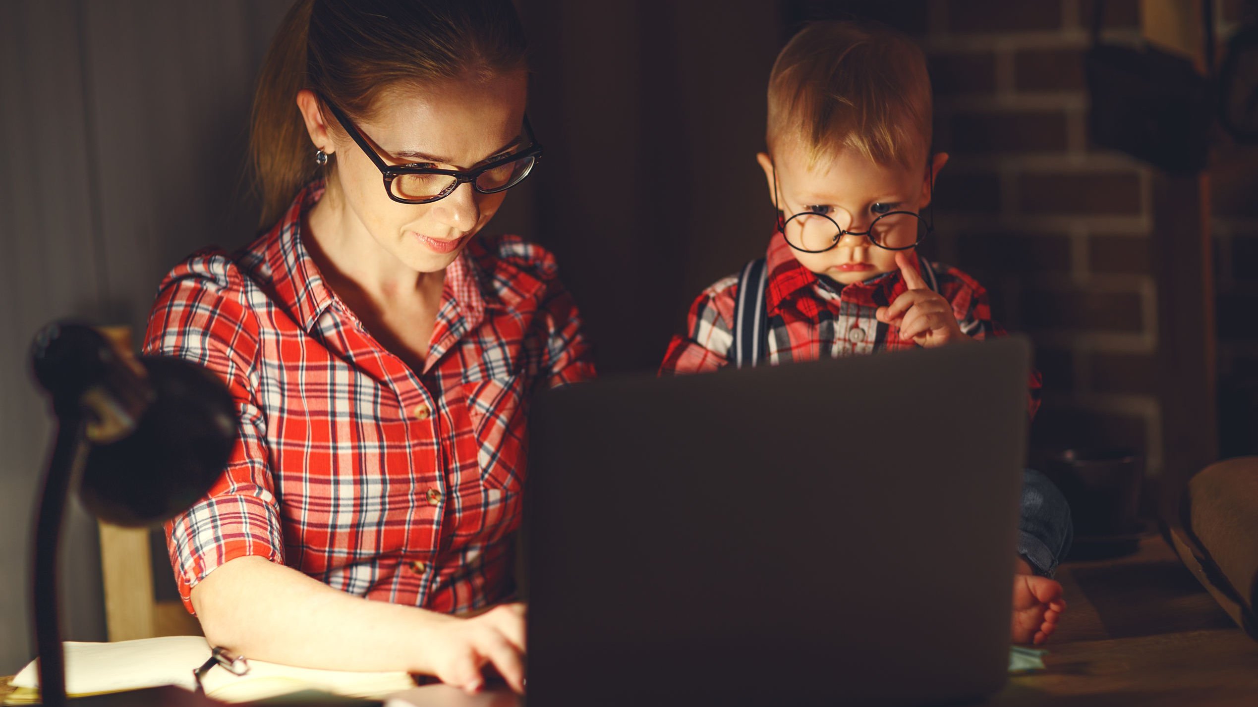 Mulher digitando em computador com bebê ao lado