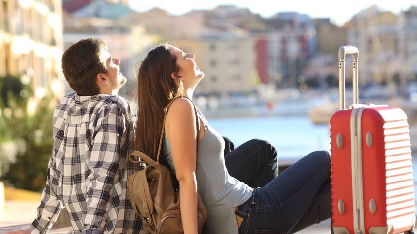 Casal  com uma mala sentados na calçada relaxando