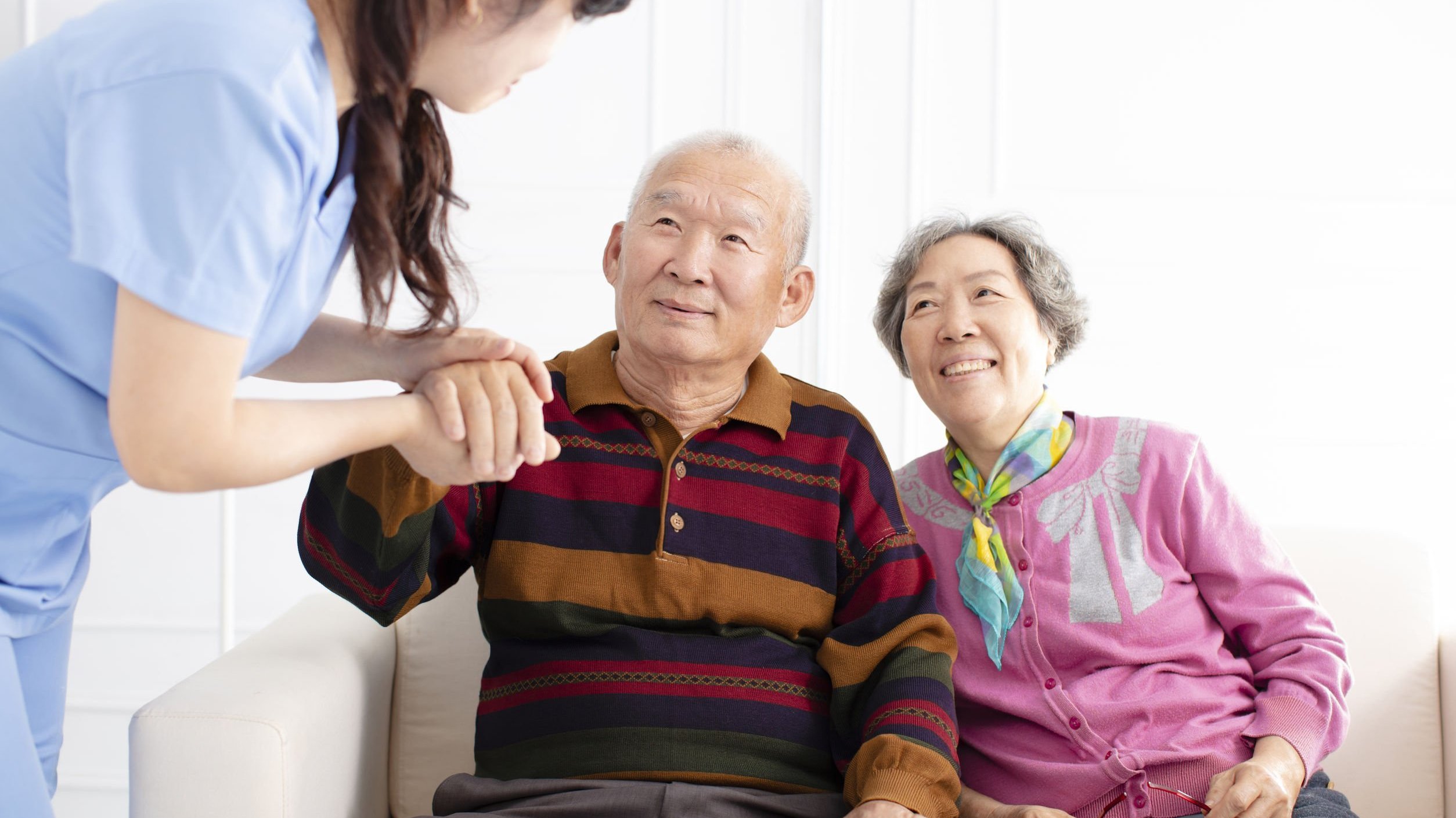 Enfermeira ajudando dois idosos asiáticos, sorridentes, que estão sentados