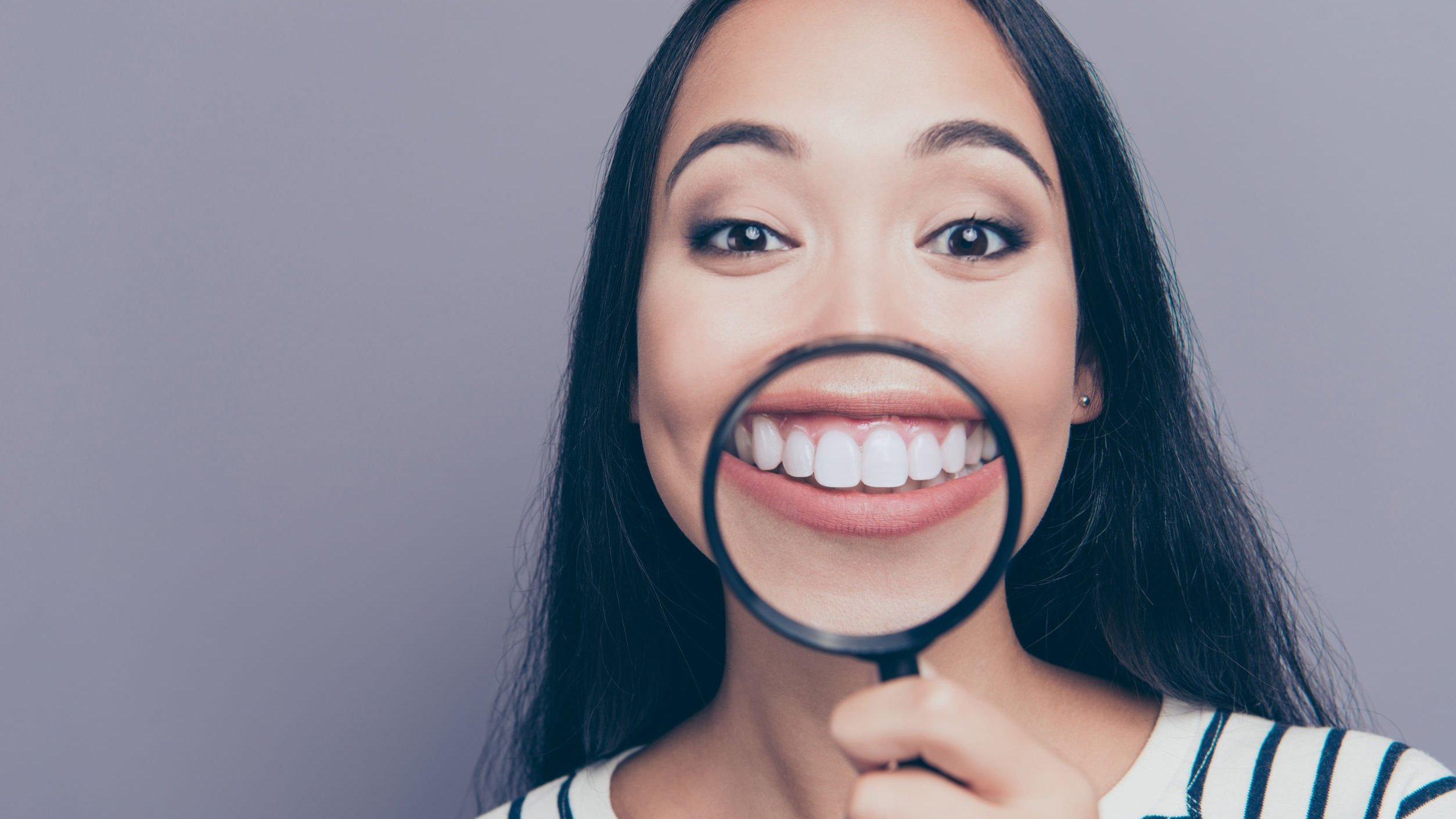 Menina jovem sorrindo com uma lupa focando em seus dentes