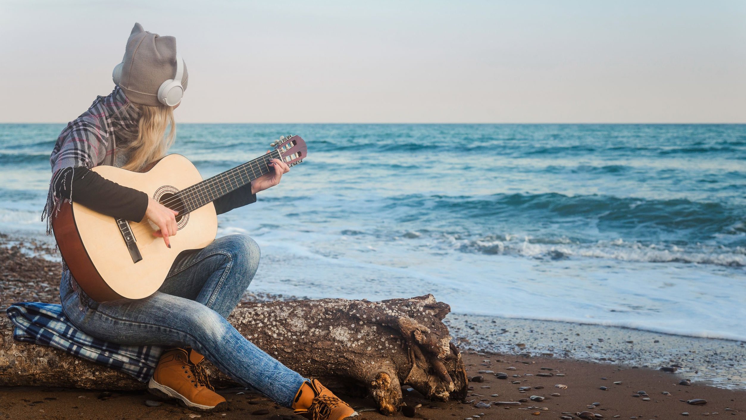 Mulher tocando violão, de frente pro mar.