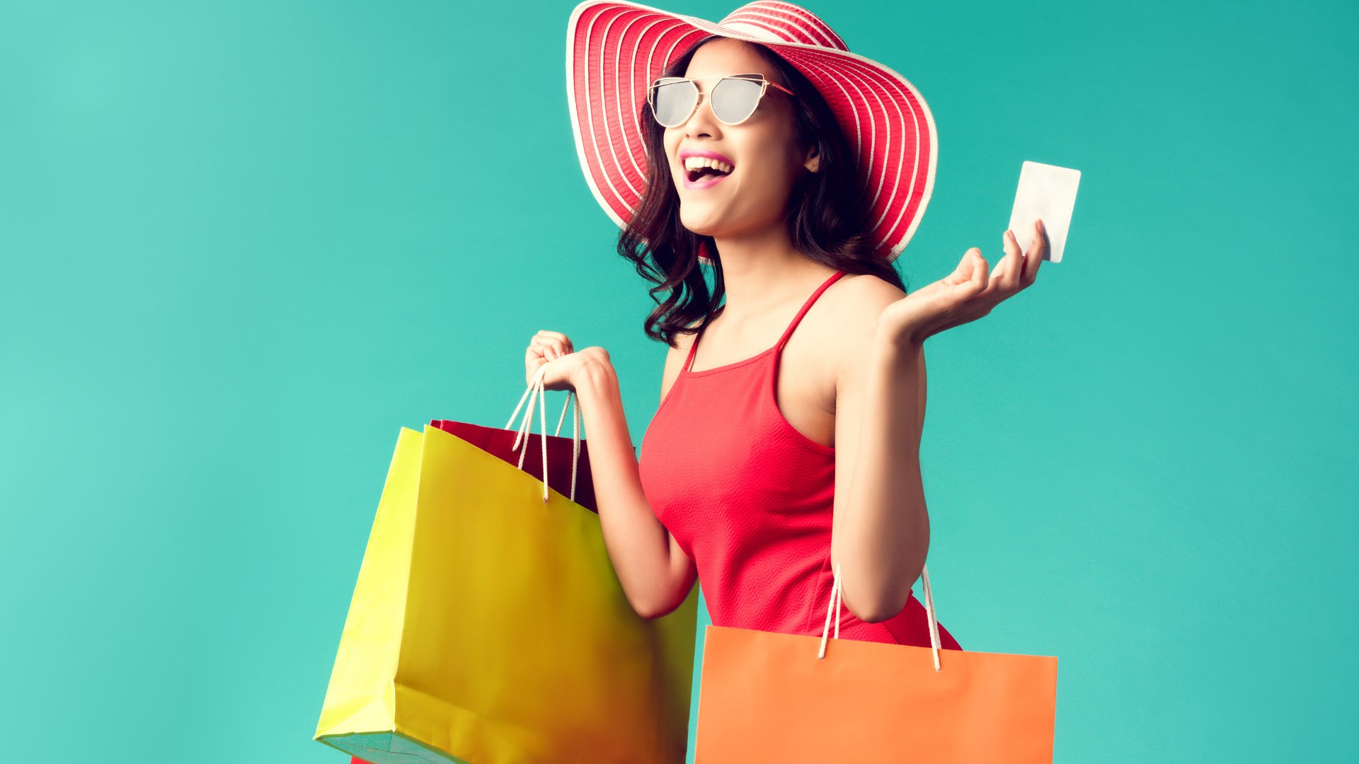 Mulher usando óculos de sol e chapéu sorrindo enquanto segura várias sacolas de compra