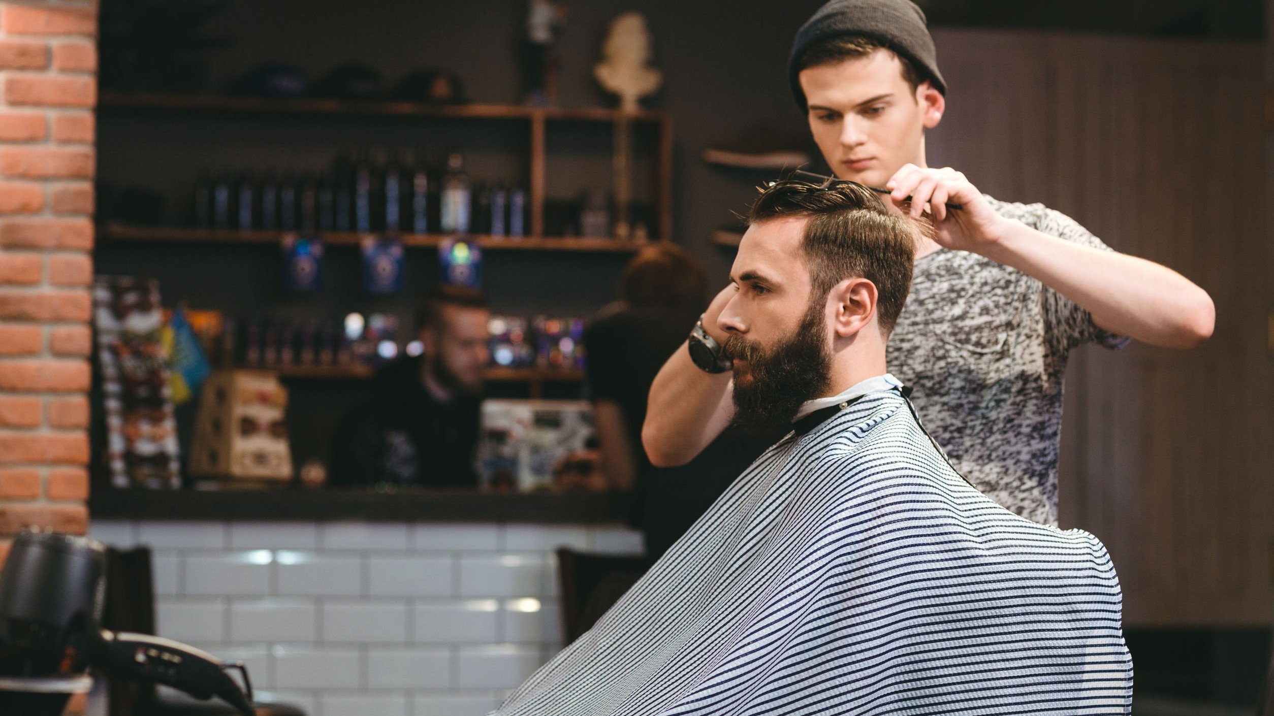 Cabeleireiro cortando cabelo de cliente sentado em cadeira.