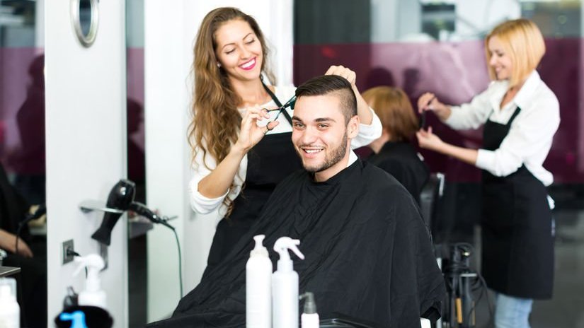 Cabeleireira cortando o cabelo de um homem no estúdio de cabeleireiro