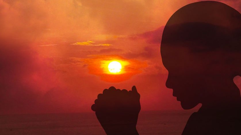 Sombra de uma mulher rezando ao pôr do sol