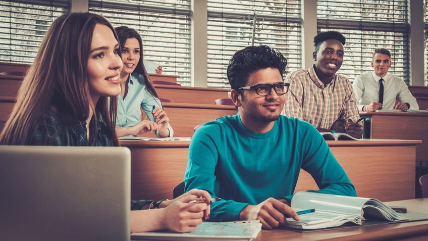 Grupo de alunos participando de uma aula sentados em uma sala de aula.