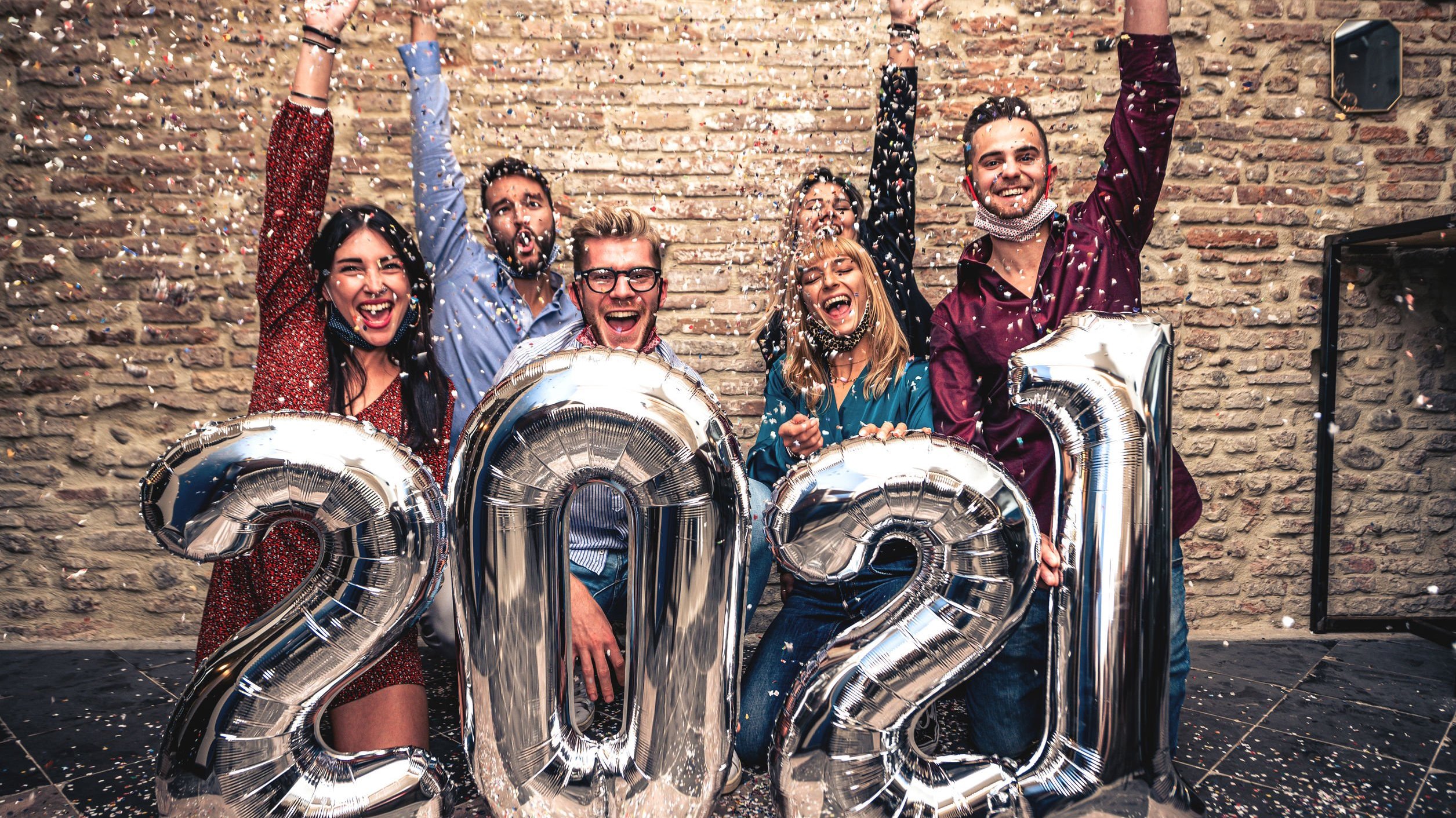 Grupo de amigos comemora o ano novo em frente a balões de número 2021.