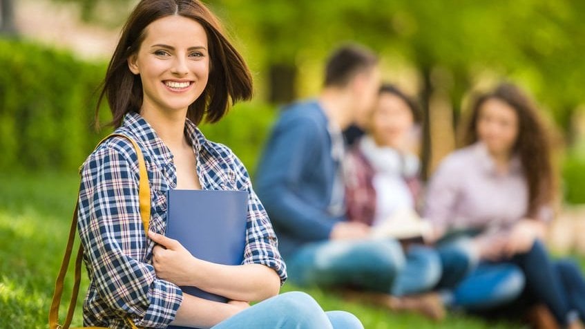 georgerudy / 123rf Menina sorrindo com caderno no colo e amigos ao fundo