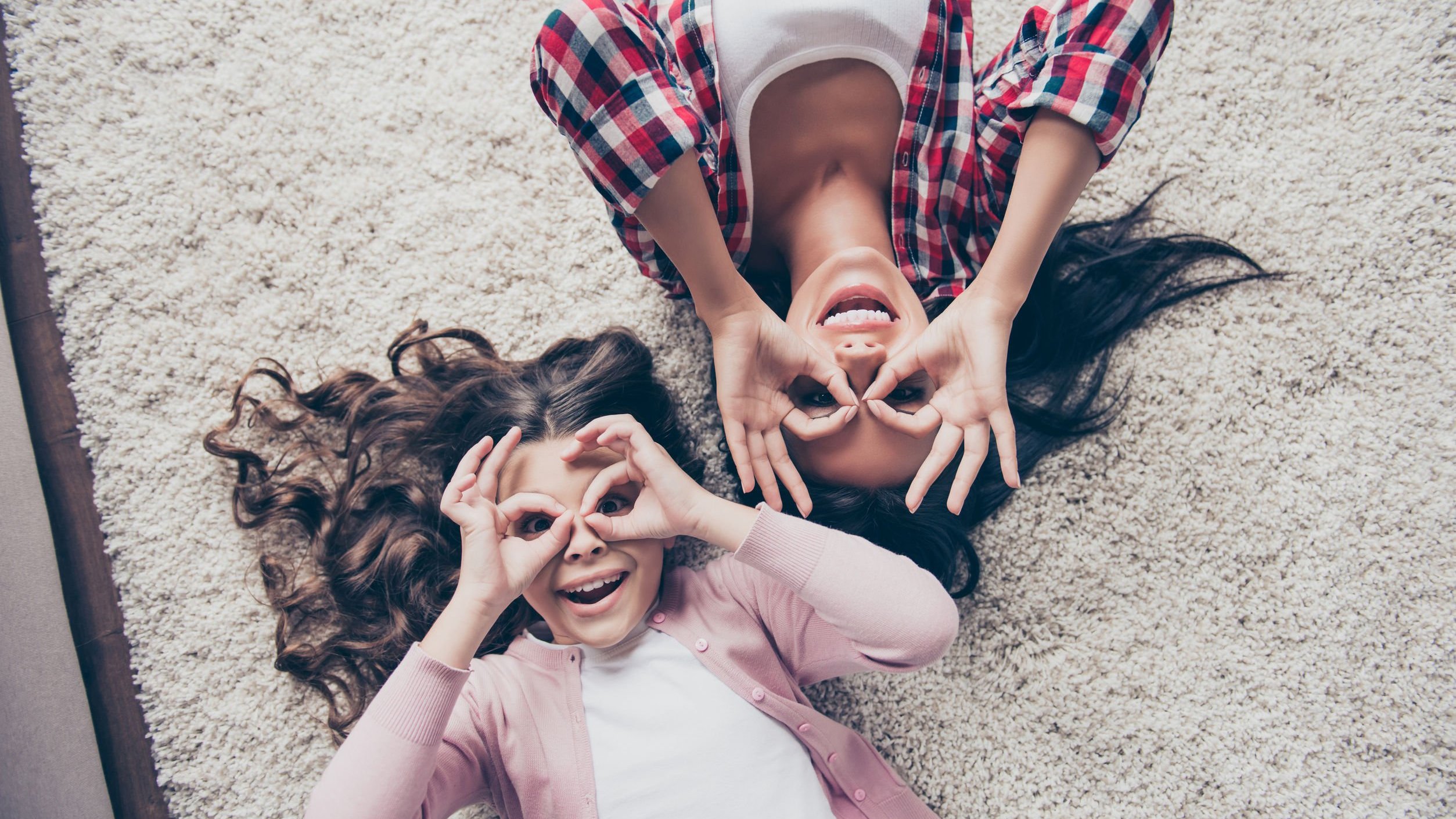 Mãe e filha, deitadas em tapete sorrindo, com as mãos nos olhos.