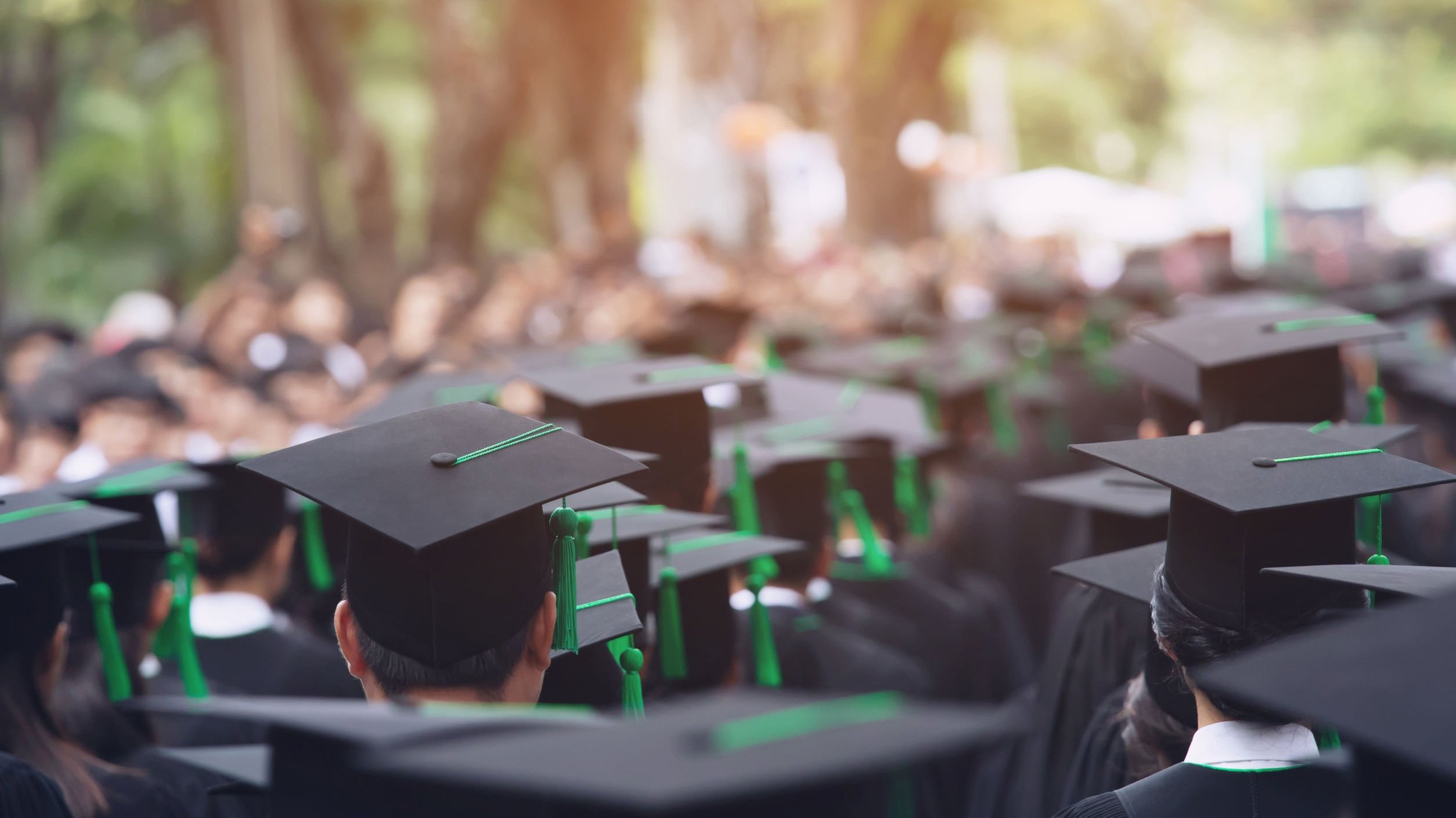 Grupo de pessoas usando capelo e beca sentados em cerimônia de formatura