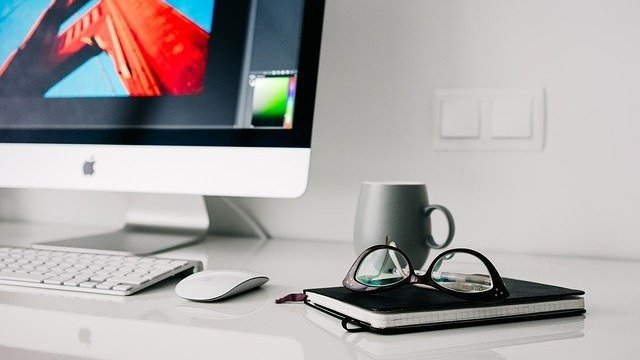 Mesa com computador, caderno e óculos em cima