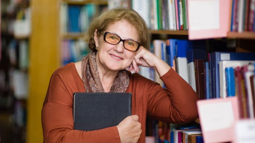 Mulher sorrindo com cotovelo apoiado em estante de livros