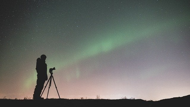 Homem com telescópio e aurora boreal ao fudno