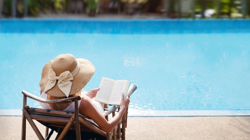 Mulher lendo livro em frente a piscina