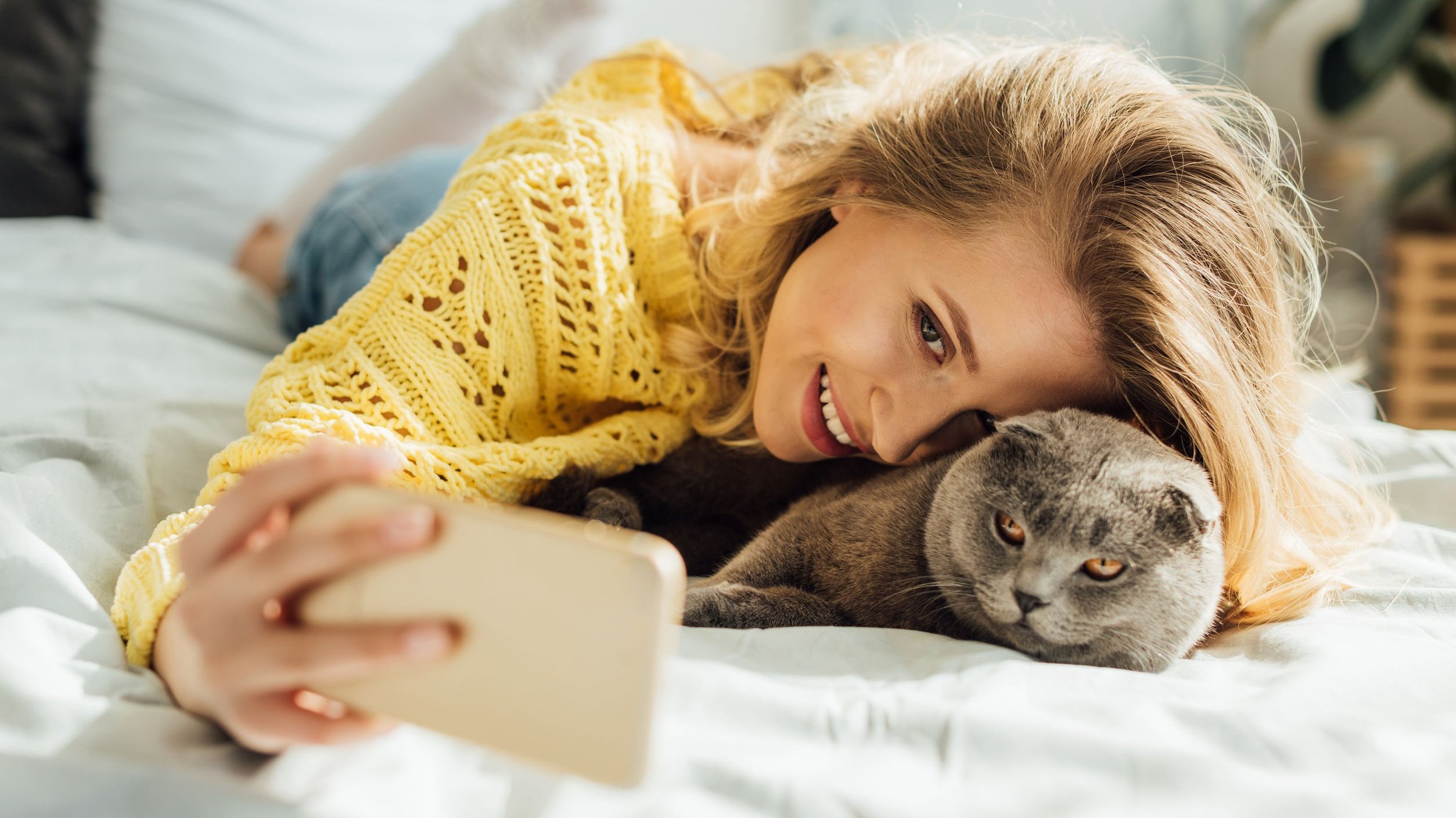 Mulher deitada em cama, tirando selfie com gato.