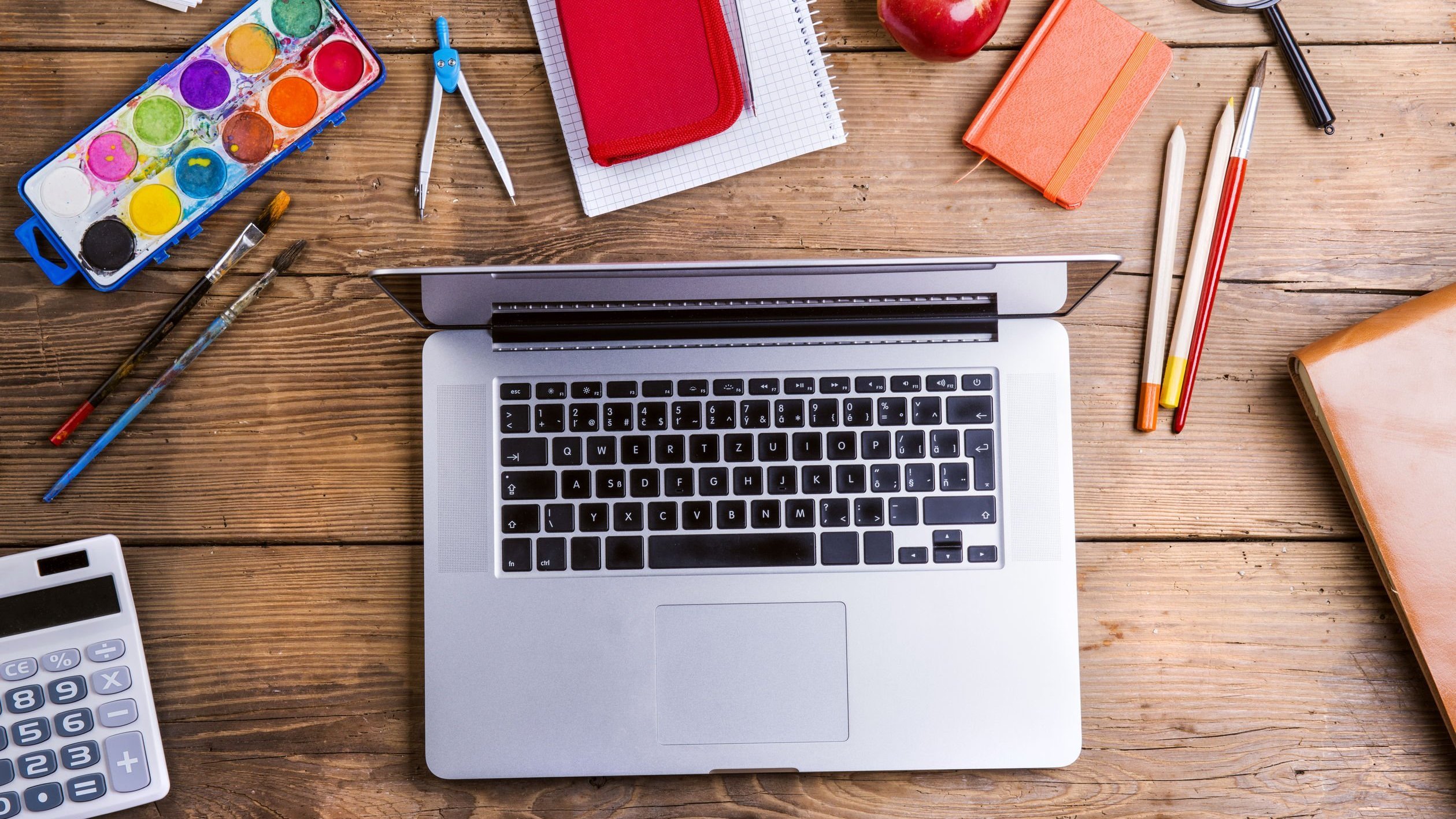 Laptop aberto em uma mesa com materiais de escola