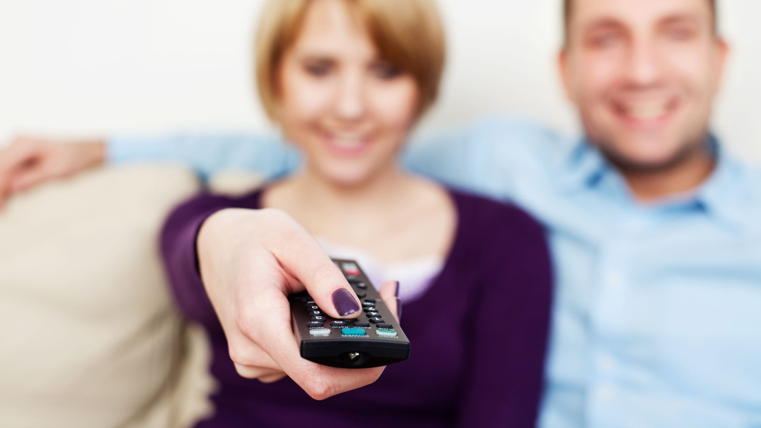 Mulher segurando controle de tv, sentada ao lado de homem sorrindo.