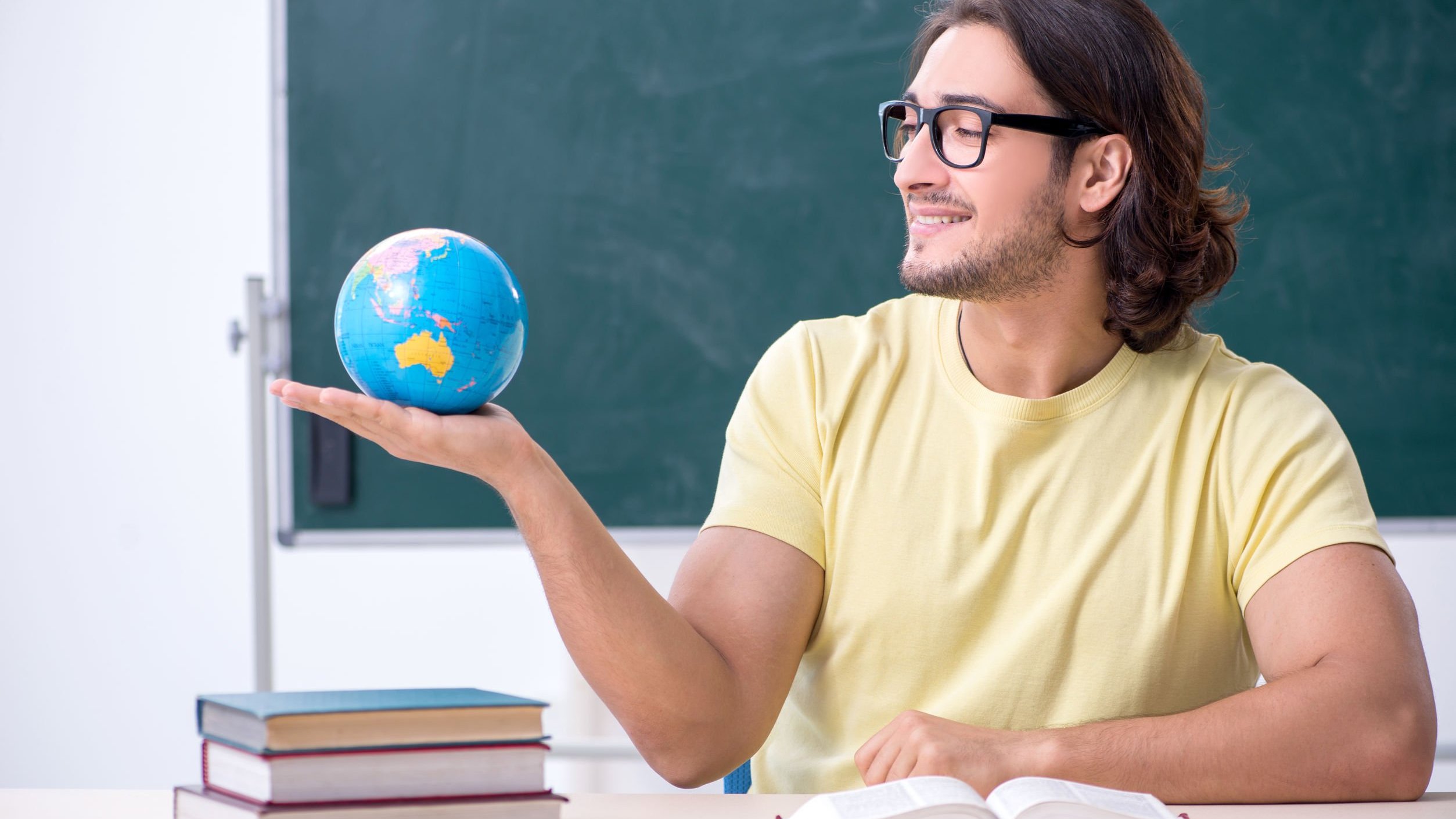 Homem geografo, sorrindo, segurando globo terrestre.