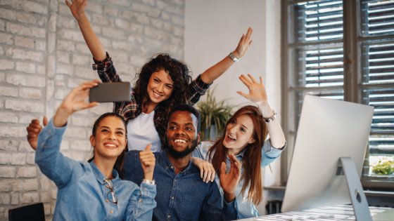 Djiledesign / Canva Colegas de trabalho na mesa tirando selfie