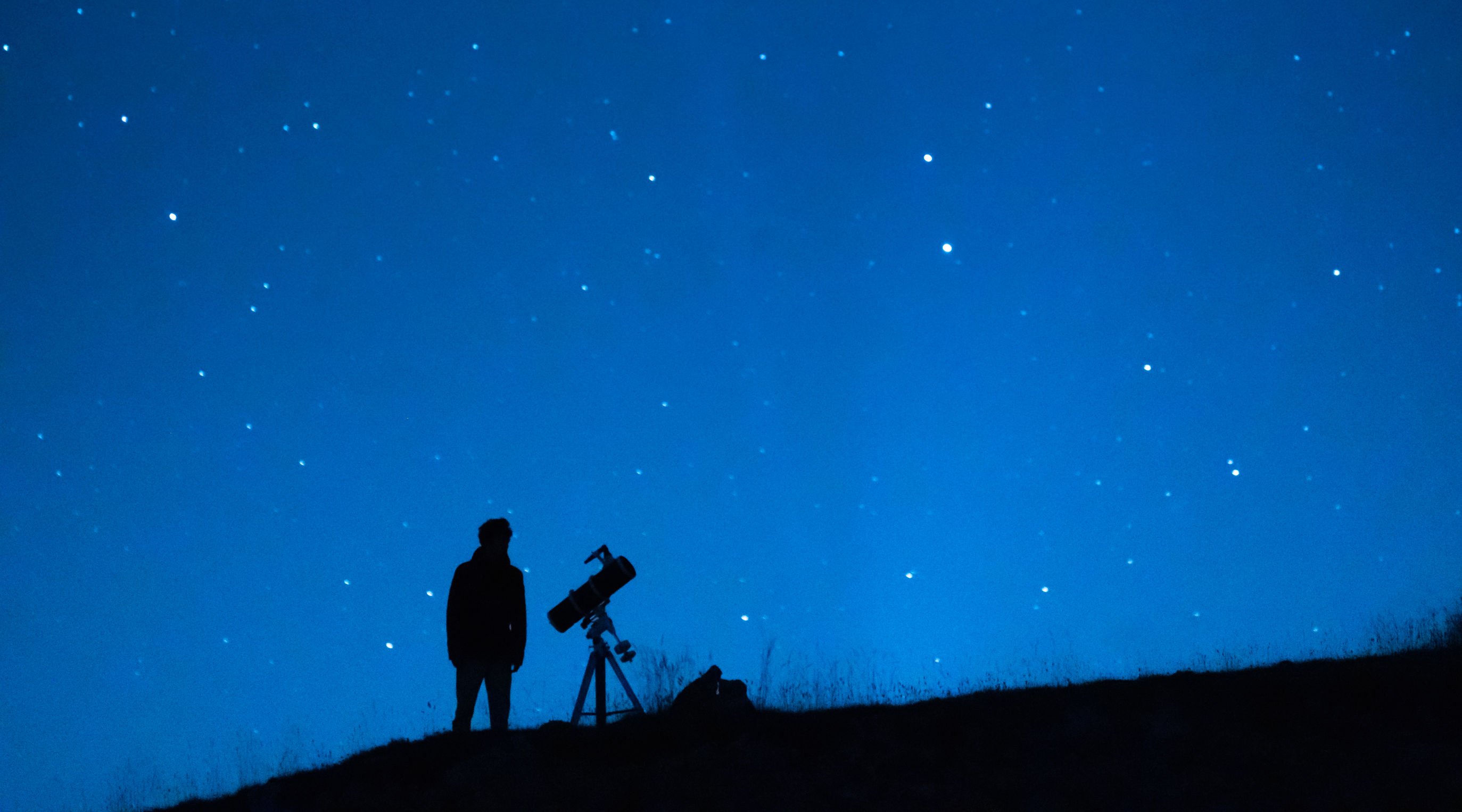 Silhueta de homem junto de telescópio.