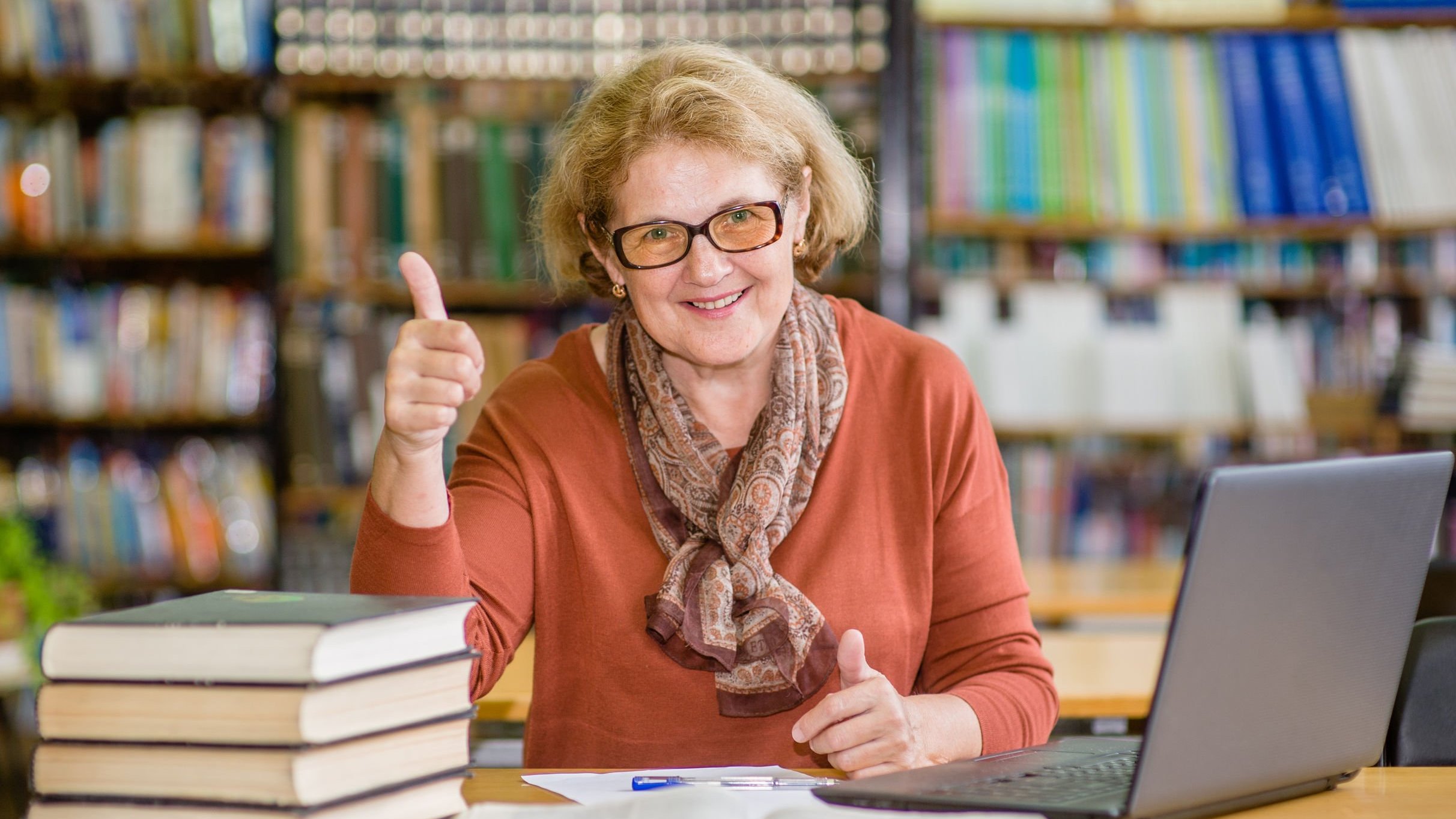 Mulher bibliotecária fazendo joia com a mão e sorrindo.