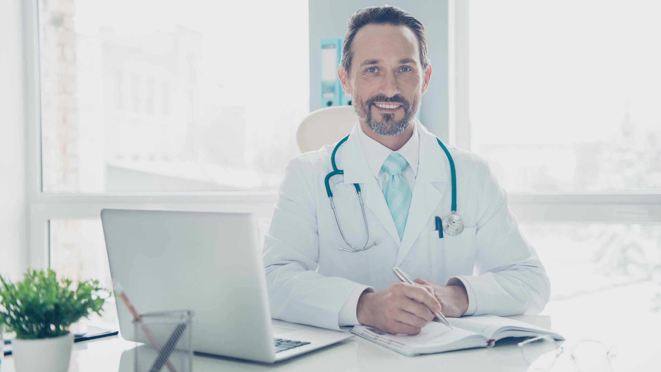 Médico sorrindo sentado em mesa de consultório