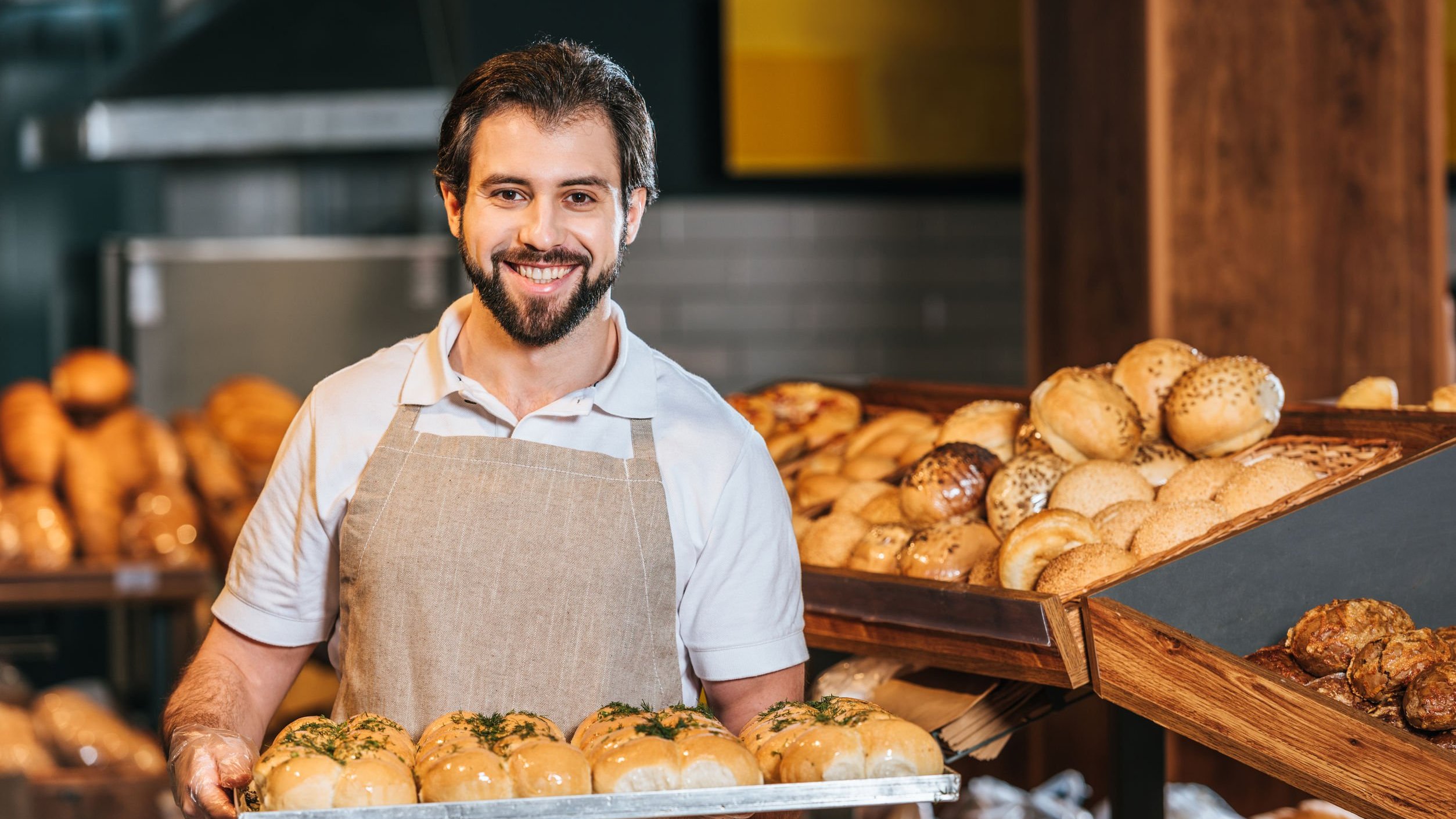 Padeiro sorrindo, segurando bandeja com pães.