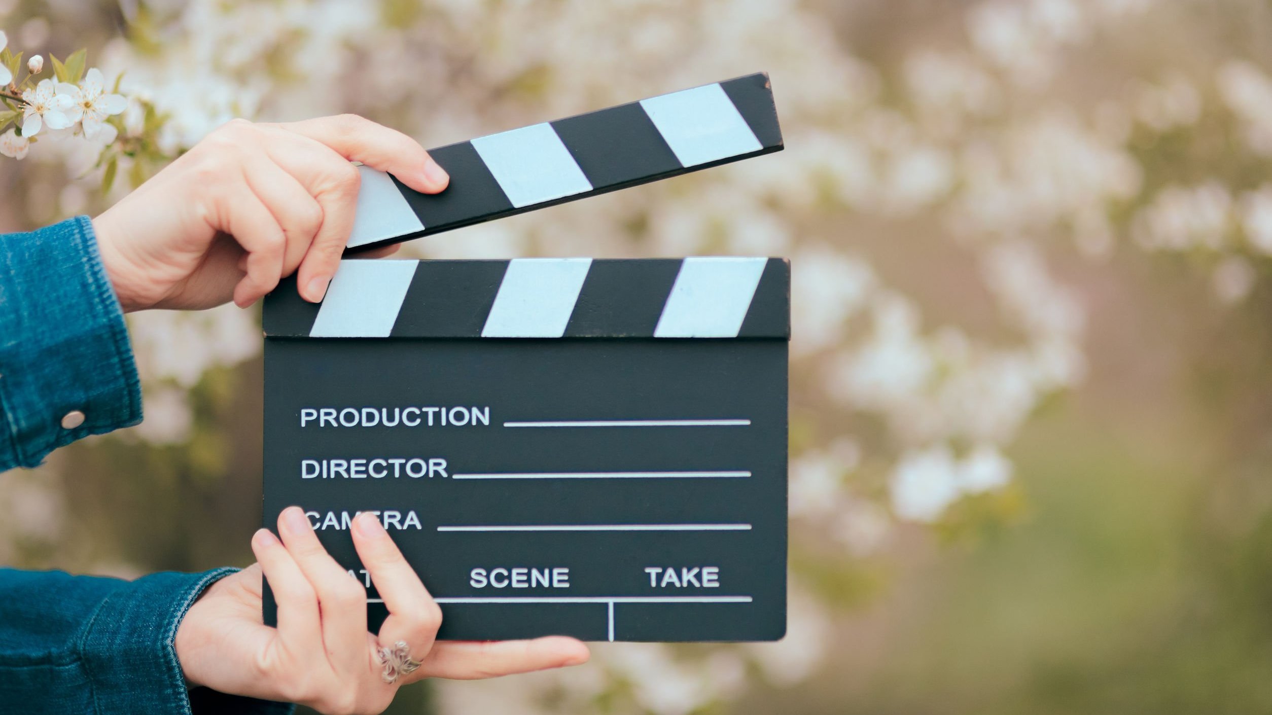 Mãos segurando um filme de ardósia de cinema em fundo de primavera florescendo.