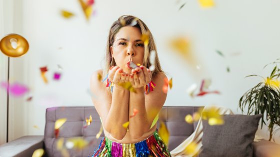 Mulher assoprando confetes coloridos em sua sala