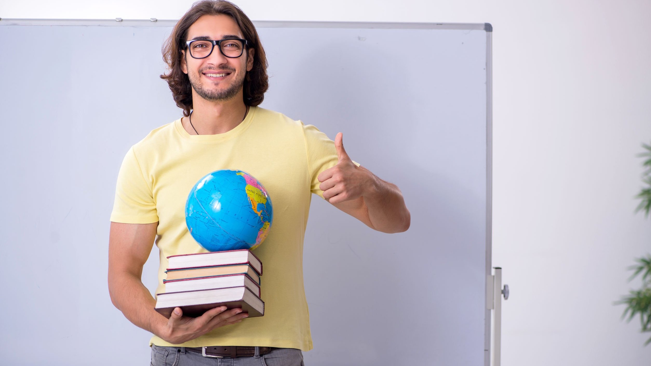 Homem geógrafo sorrindo, segurando livros e globo terrestre.