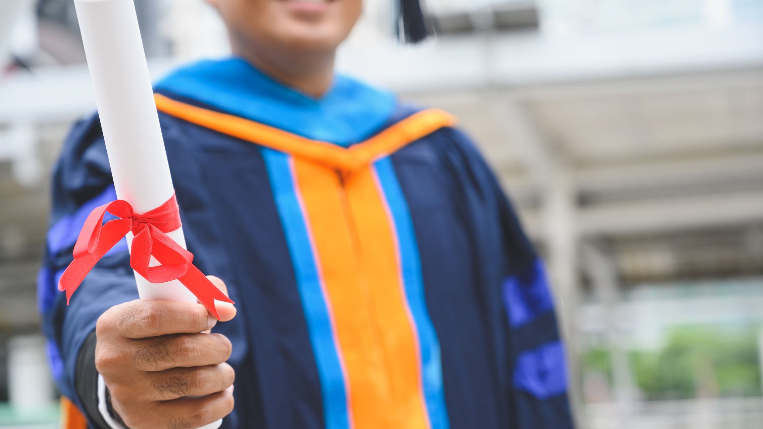 Menino vestido com roupa de formatura, segurando diploma.