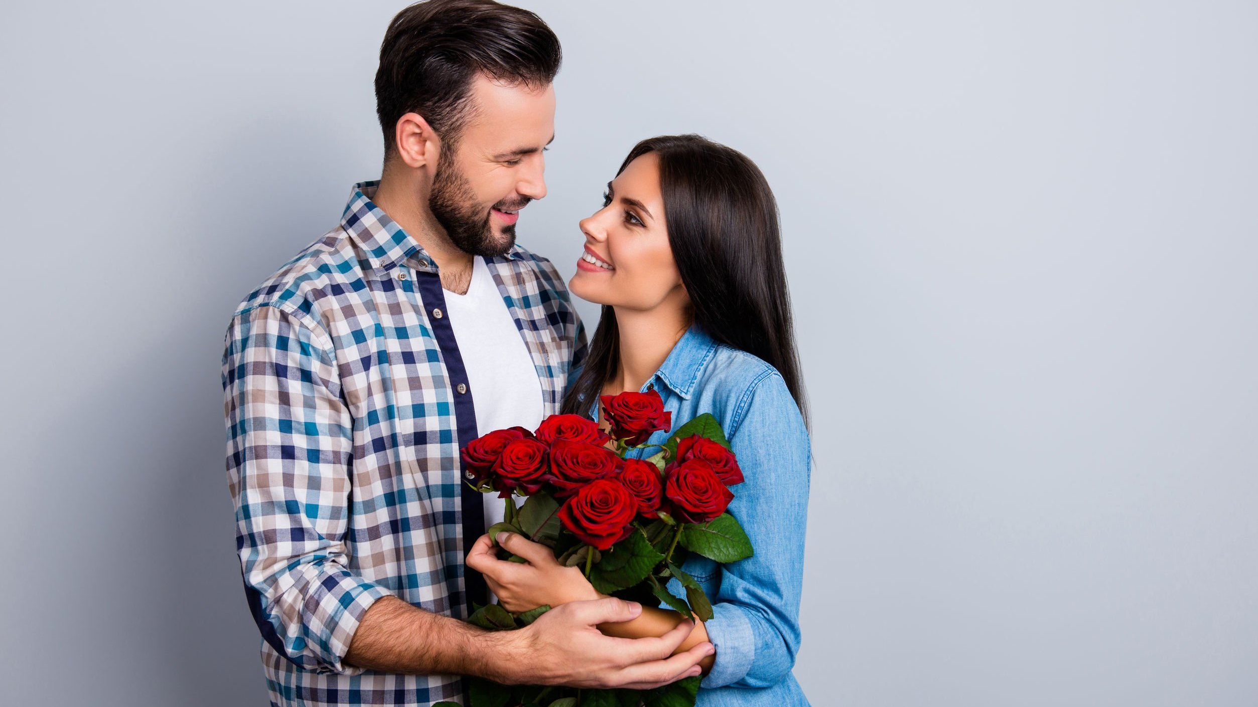 Casal se olhando, sorrindo. Mulher serurando buque de rosas.