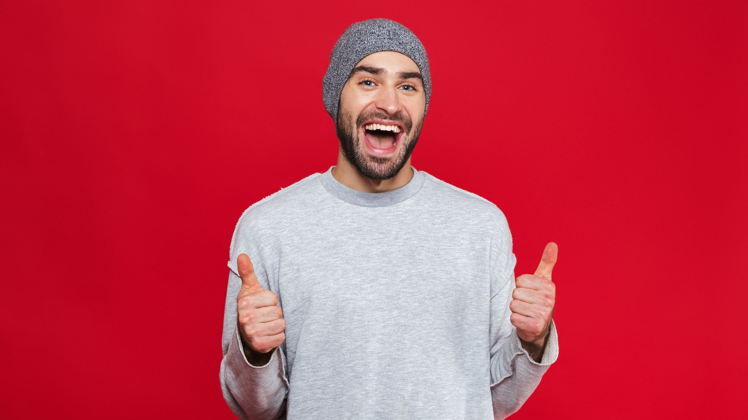 Homem sorrindo, feliz, fazendo sinal de joia com as mãos.