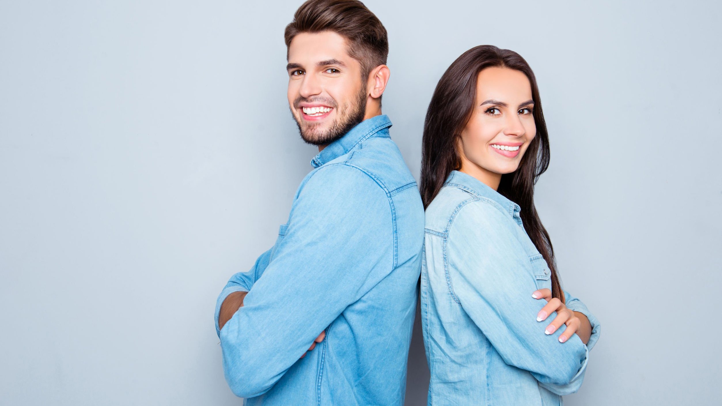 Homem e mulher, de costas um para o outro, braços cruzados e sorrindo.