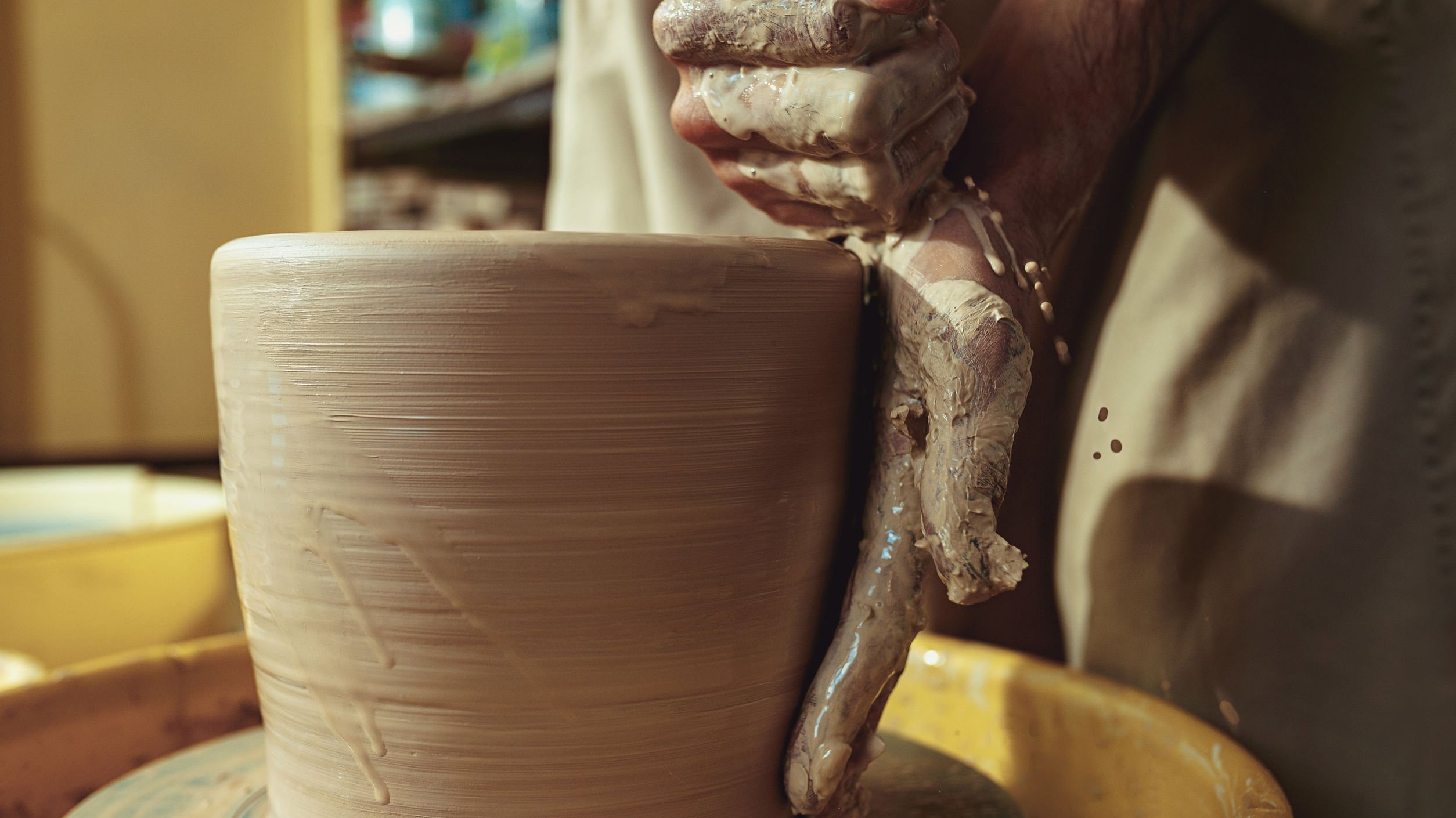 Mão de artesão moldando vaso de barro.