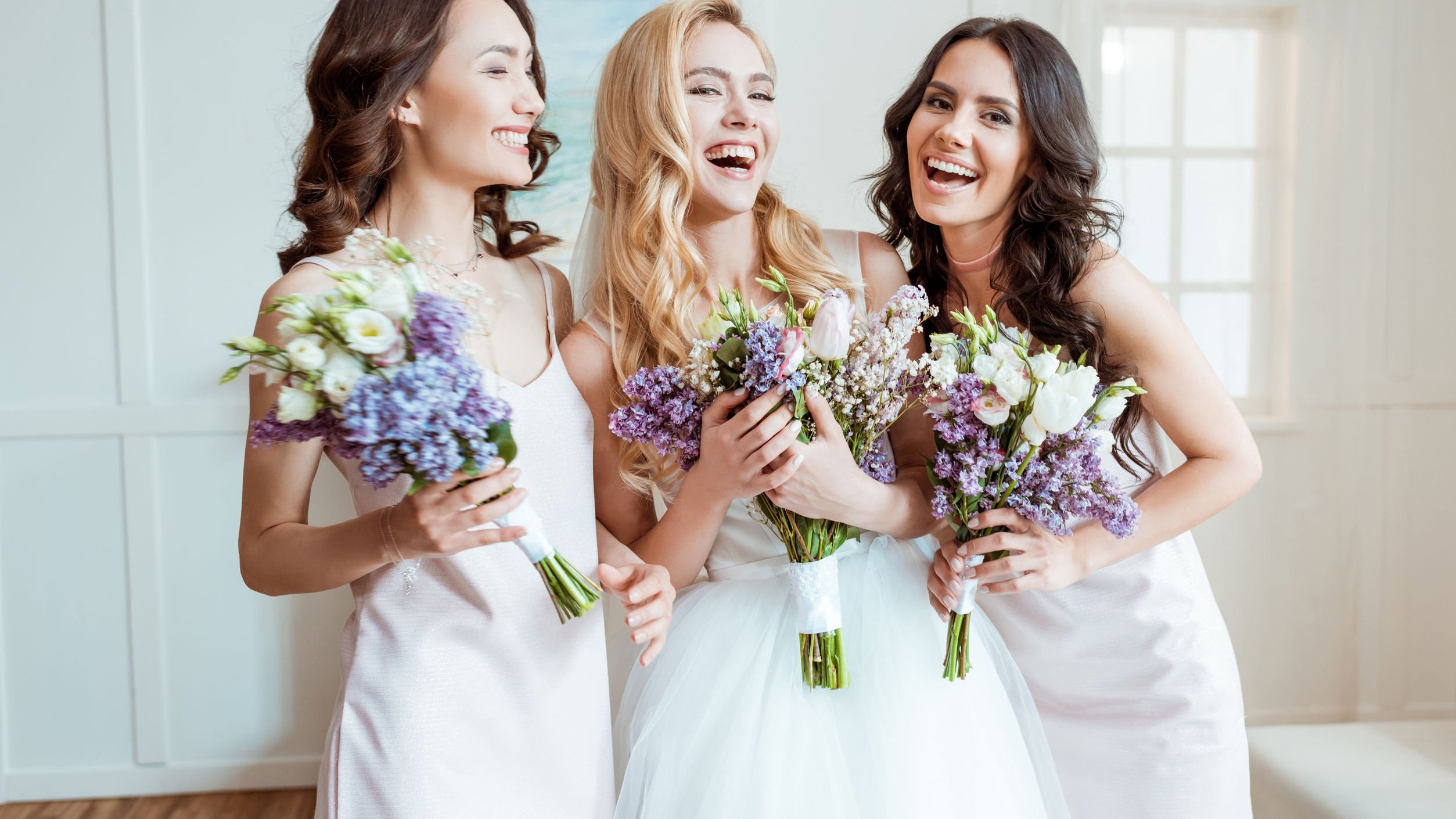 Madrinhas de casamento, sorrindo e segurando buque de flores.