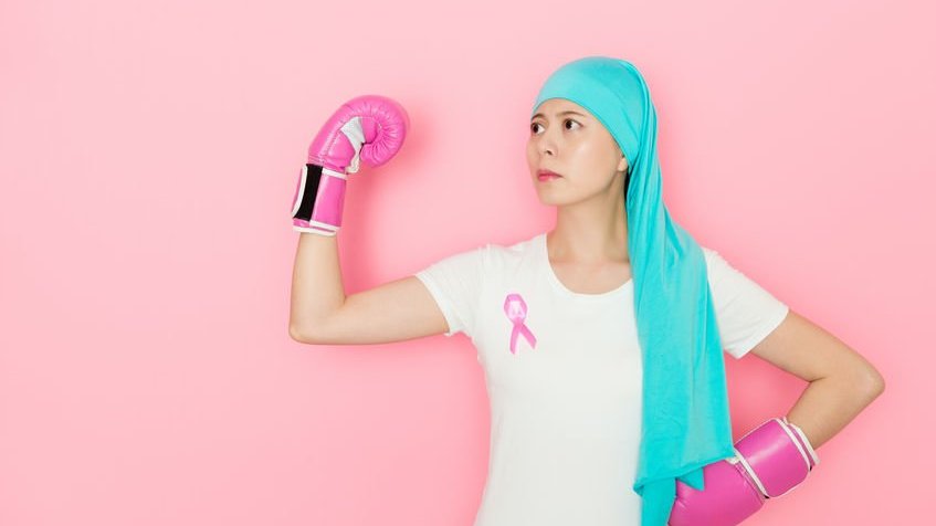 Mulher com luvas de box e broche símbolo da luta contra o câncer de mama