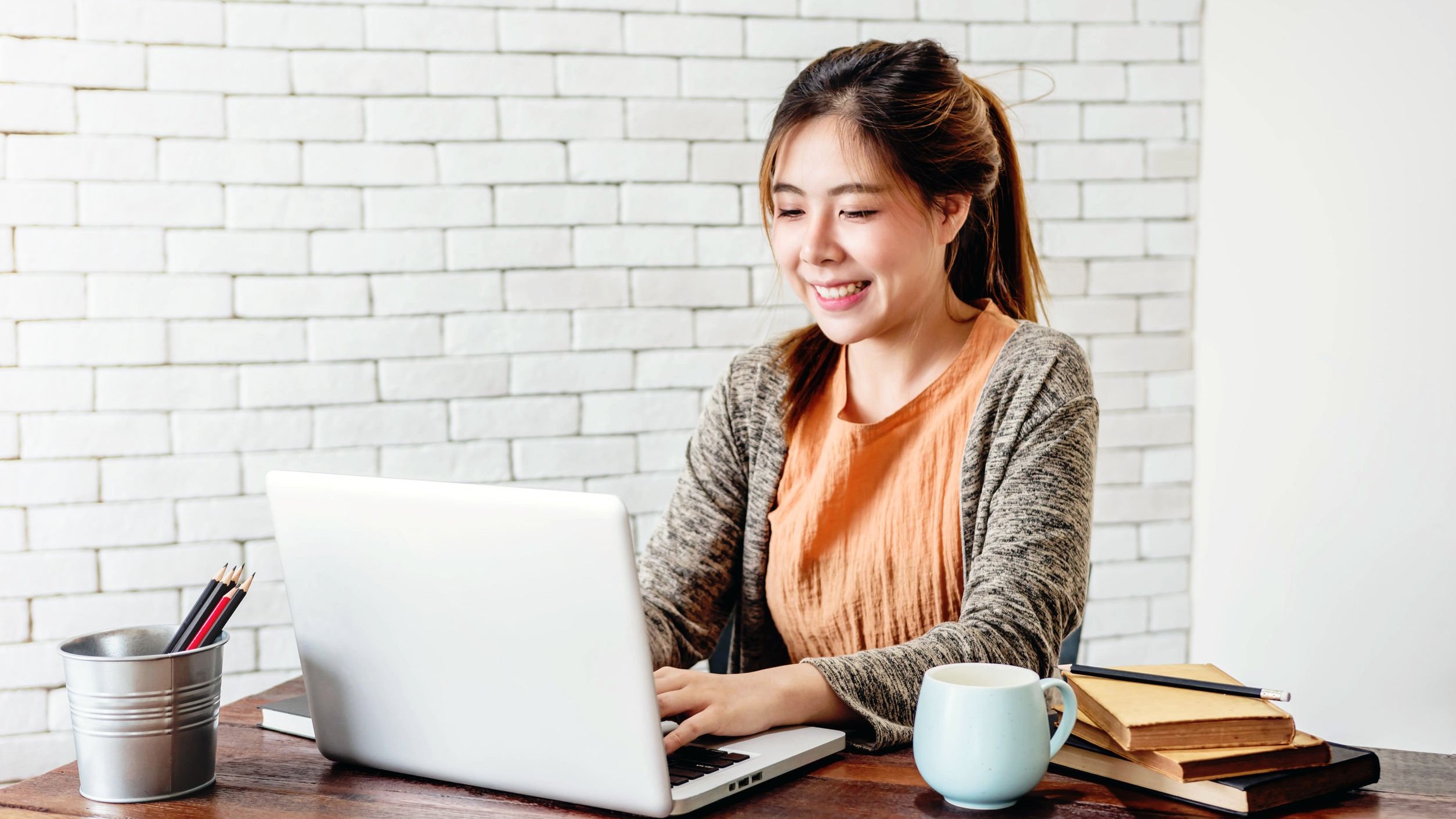 Mulher sentada sorrindo, mexendo em notebook, trabalhando em casa.