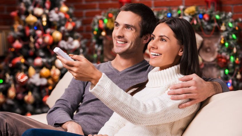 Casal assistindo TV e decoração natalina ao fundo