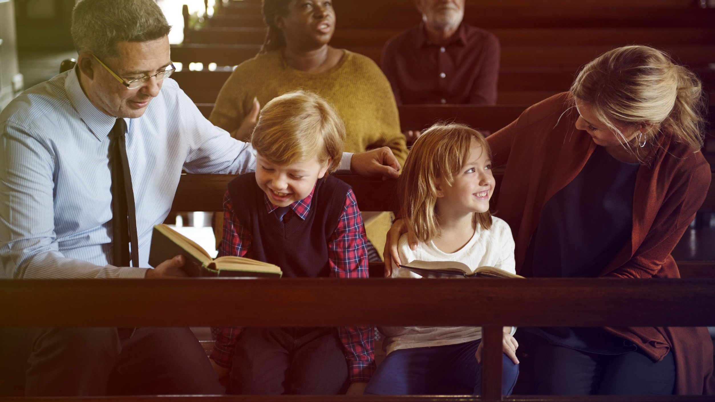 Família composta por um homem e uma mulher e duas crianças sentadas no banco de uma Igreja