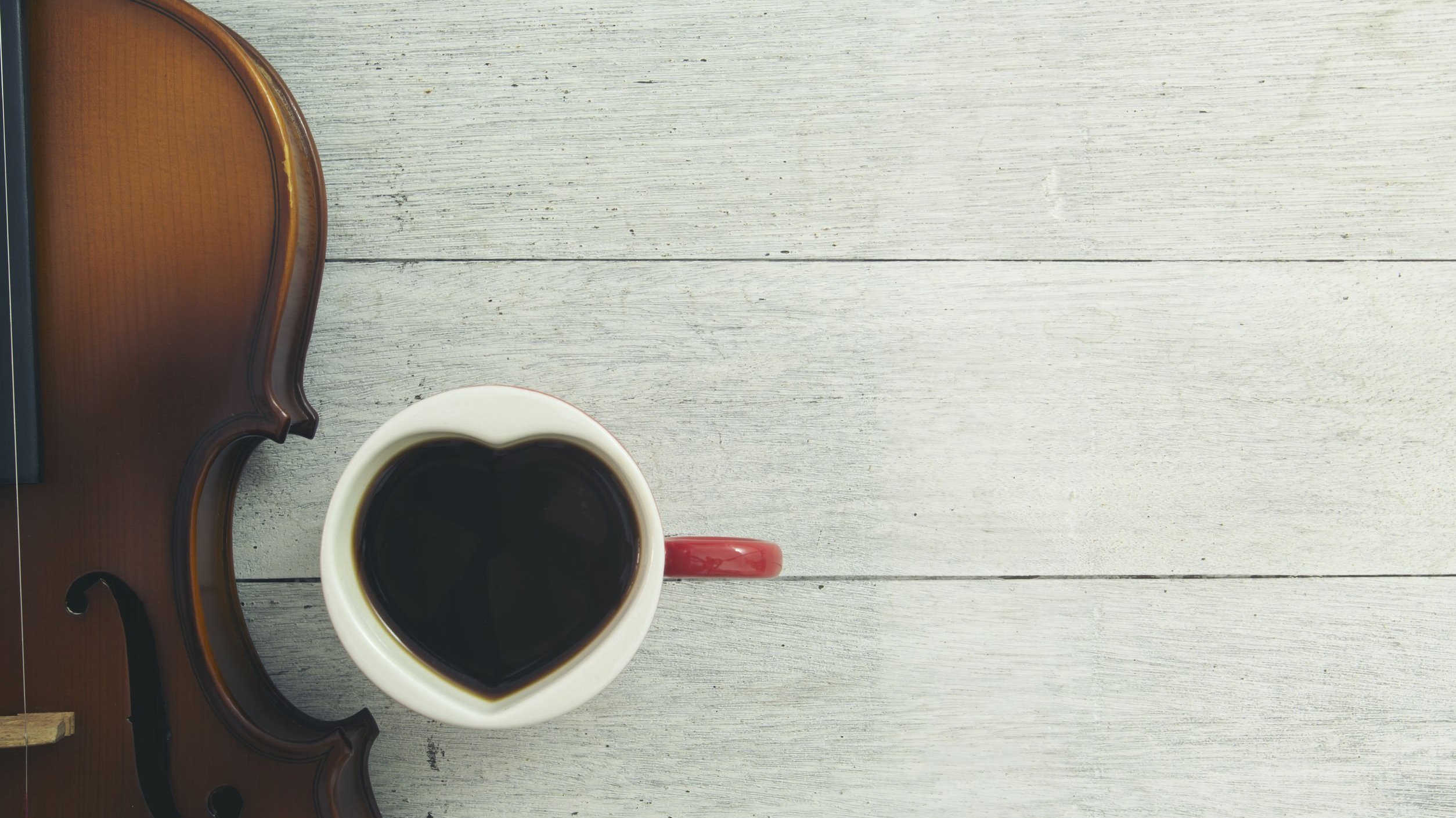 Violino marrom com xícara de café em formato de coração ao lado.