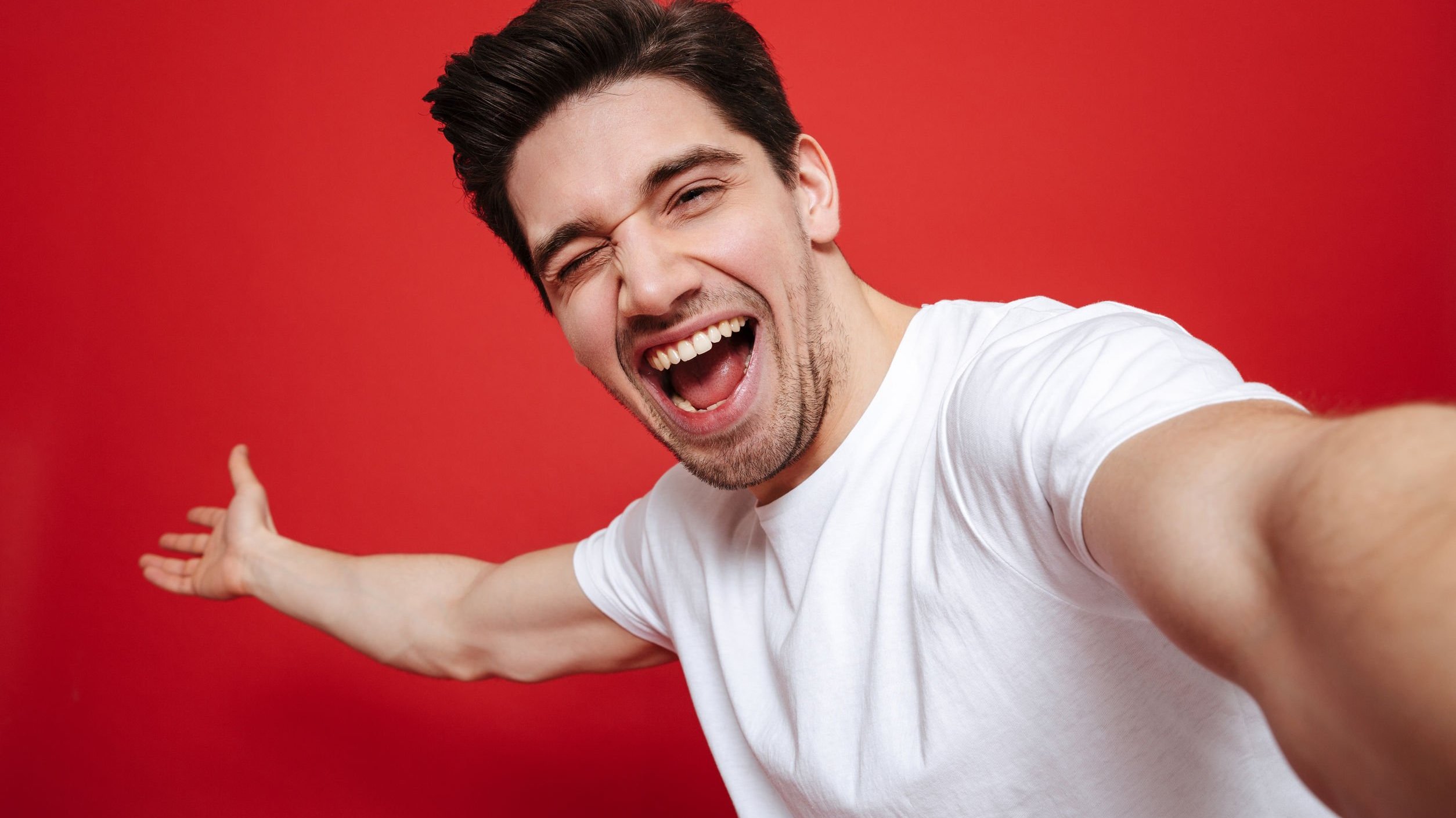 Homem tira selfie sorrindo em fundo vermelho.