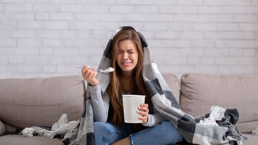 Menina chorando em sofá e comendo pote de sorvete