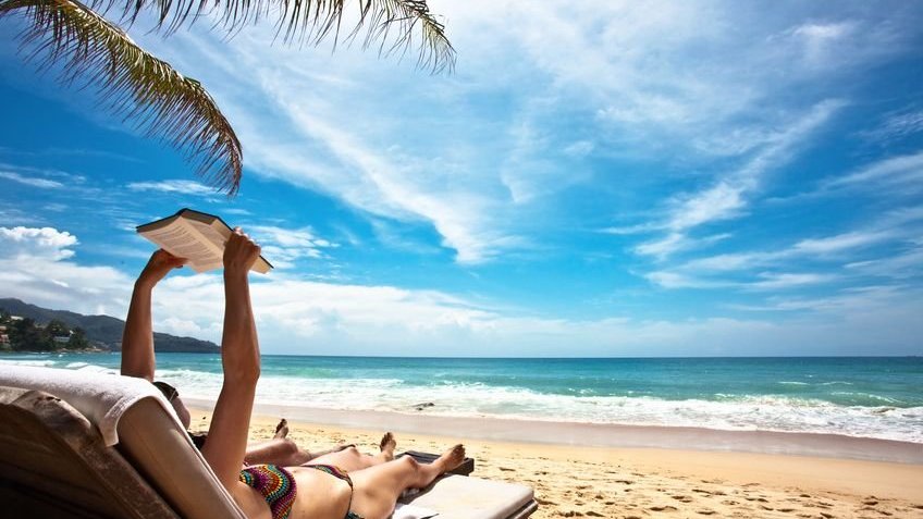 Mulher deitada em praia lendo livro