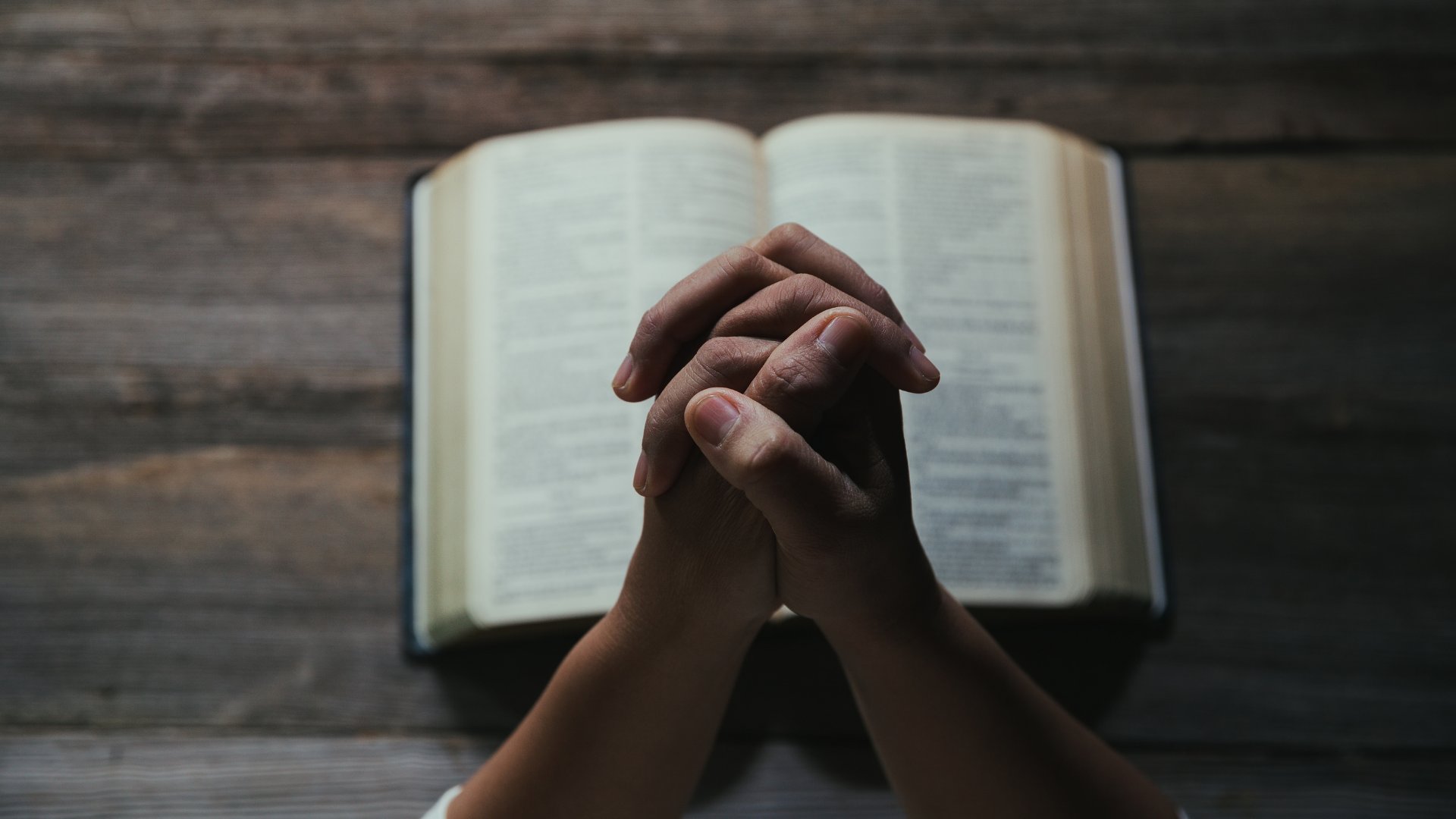 Pessoa com as mãos unidas orando sobre a bíblia