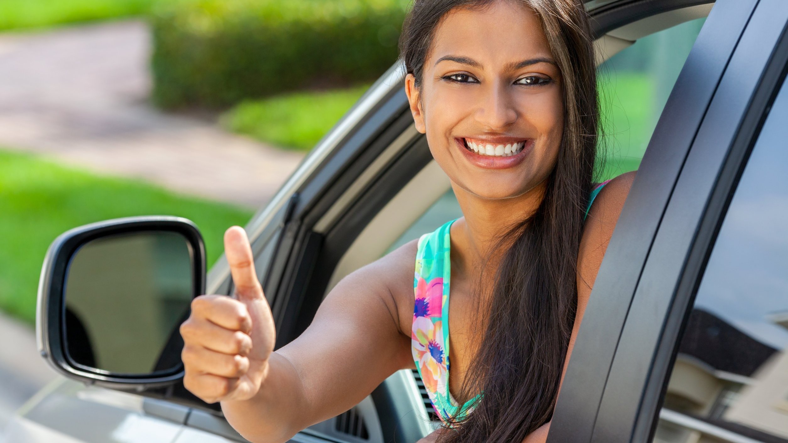 Mulher dentro de carro sorri. Ela ergue o polegar em sinal positivo.